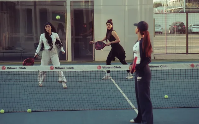 Joueuses de padel en plein échange près du filet sur un court vitré