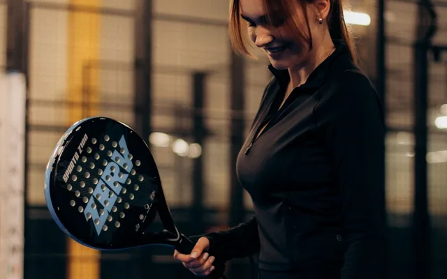 Joueuse souriante tenant une raquette de padel sur un court vitré